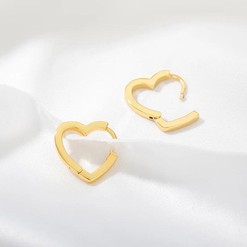 Chunky gold huggie earrings shaped like hearts, with a glossy finish and a secure snap-lock closure, resting on a white fabric.