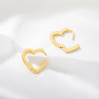 Chunky gold huggie earrings shaped like hearts, with a glossy finish and a secure snap-lock closure, resting on a white fabric.