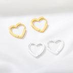 Chunky huggie earrings featuring heart-shaped designs in gold and silver, resting on a soft fabric background.