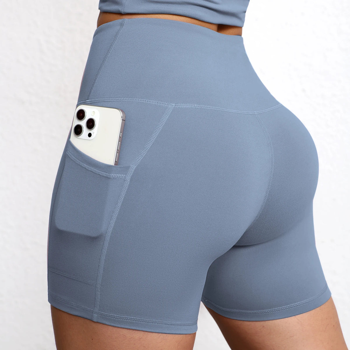 High-waisted seamless yoga shorts in light blue with integrated side pockets, showing a smartphone tucked securely in one.