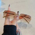 Rimless Y2K rectangle sunglasses with gradient brown lenses and gold metallic accents held in a hand with long nails.