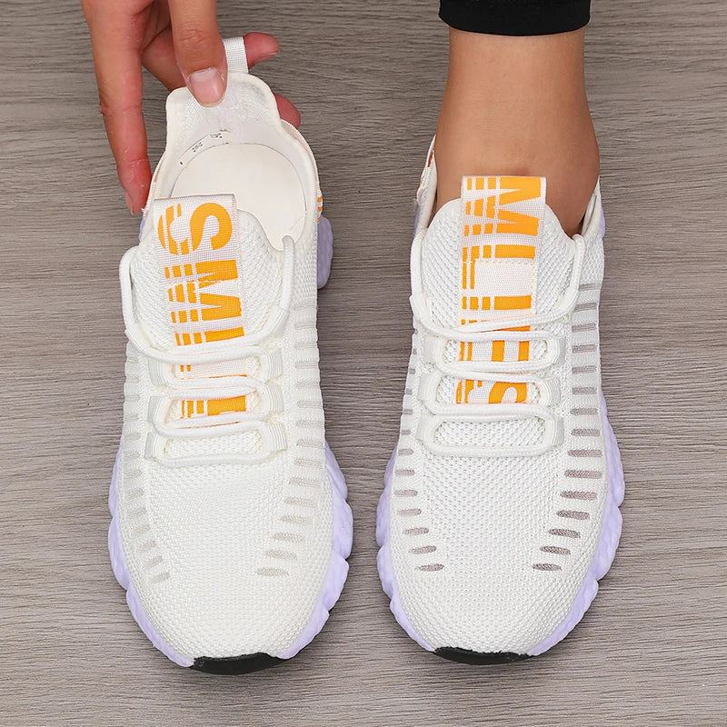Lightweight white knitted performance sneakers with orange text, featuring a flexible outsole and slip-on fit.