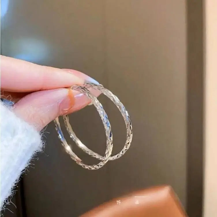 Chunky minimalist hoop earrings with a high-gloss polished finish, held between fingers, showcasing a hollow tubular design.