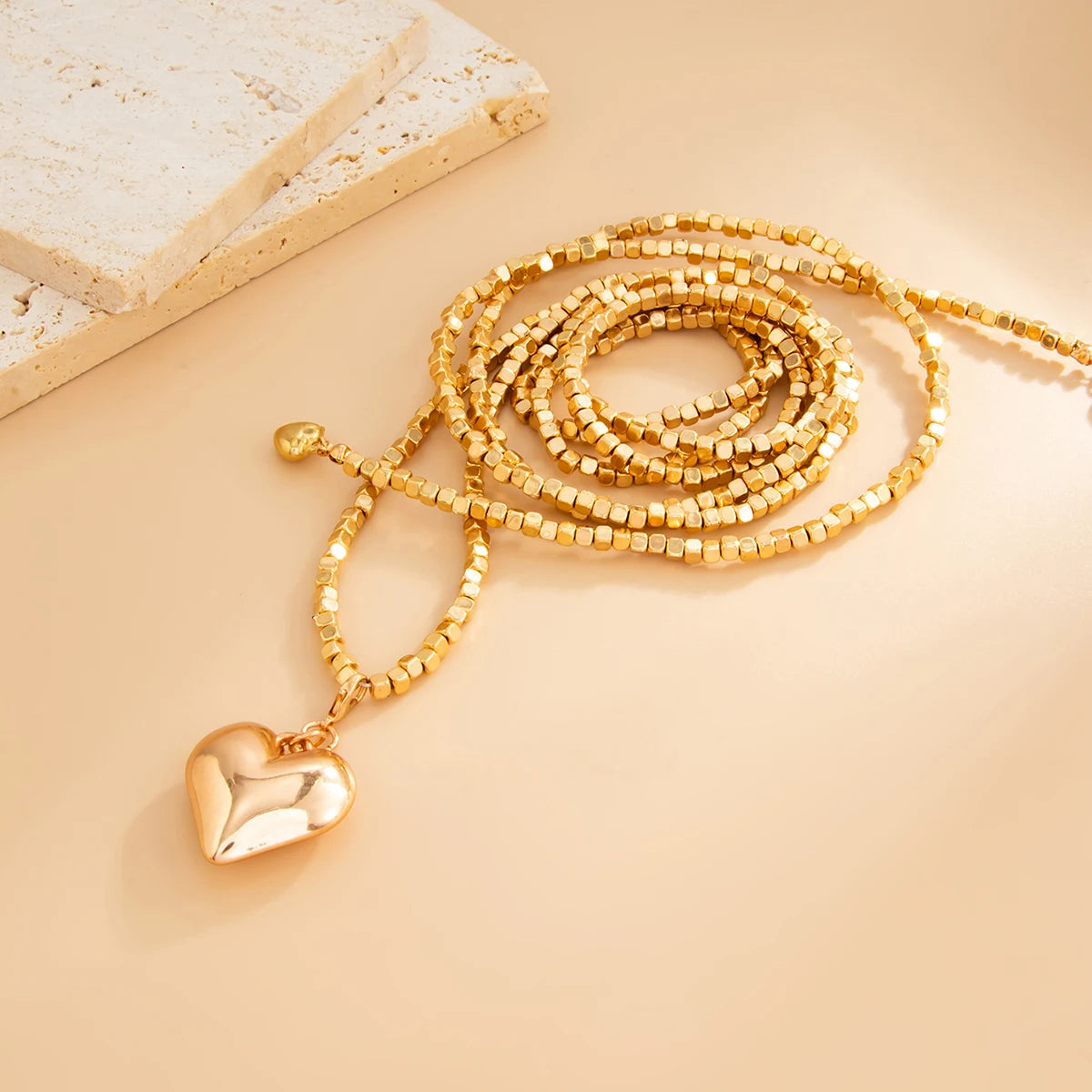 Vintage layered necklace featuring gold beaded strands and a heart pendant, resting on a smooth, neutral background.