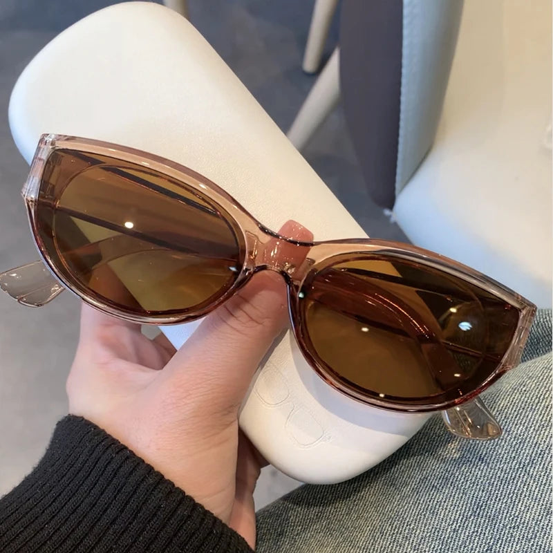 Cat-eye sunglasses with a vintage design, featuring a translucent pink frame and brown tinted lenses, held in a hand.