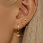 Asymmetric earring set features a gold star dangle, a hoop, and a small star stud, showcased on an ear.