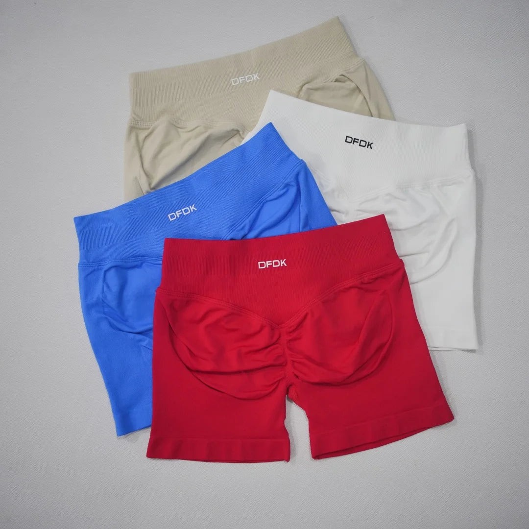 High-waisted gym shorts in four colors: cream, red, blue, and white, featuring a scrunch-butt design and branded waistband.