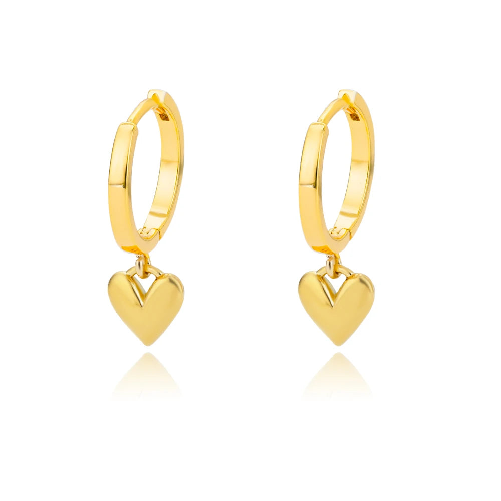 Gold huggie earrings with a chunky hoop design and a dropped heart charm, featuring a high-gloss reflective finish.