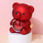 A red teddy bear holding a crystal sphere containing a red rose, displayed on a white pedestal against a pink background.
