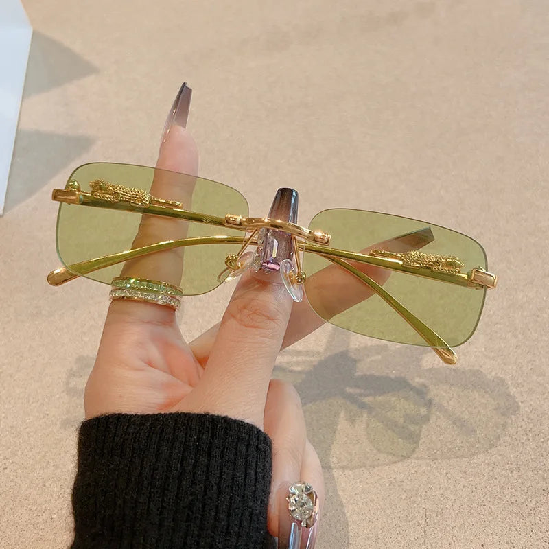 Rimless green gradient rectangle sunglasses with metallic gold accents, held between fingers, showcasing a minimalist style.