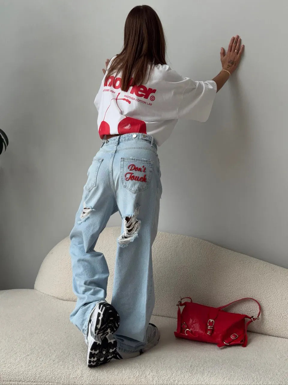 Light blue baggy distressed denim jeans with embroidered lettering detail, worn over chunky sneakers, styled with an oversized tee.