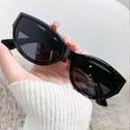 Black cat-eye sunglasses held in hand, featuring an upswept silhouette and smooth glossy finish.