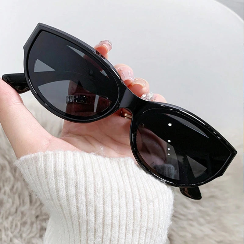 Black cat-eye sunglasses held in hand, featuring an upswept silhouette and smooth glossy finish.
