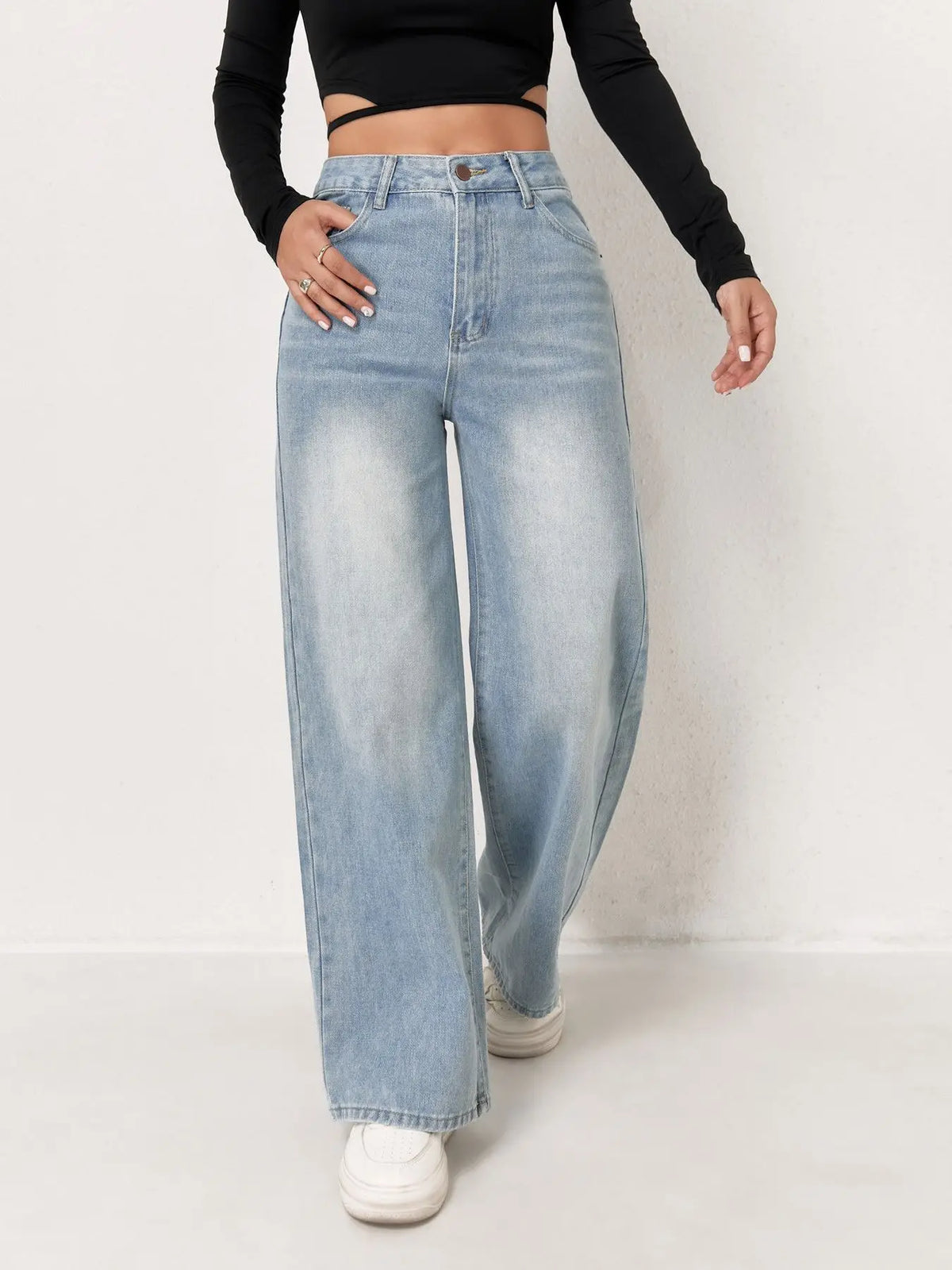 Light wash, high-waisted wide-leg denim jeans worn with a fitted black long-sleeve top and white sneakers.