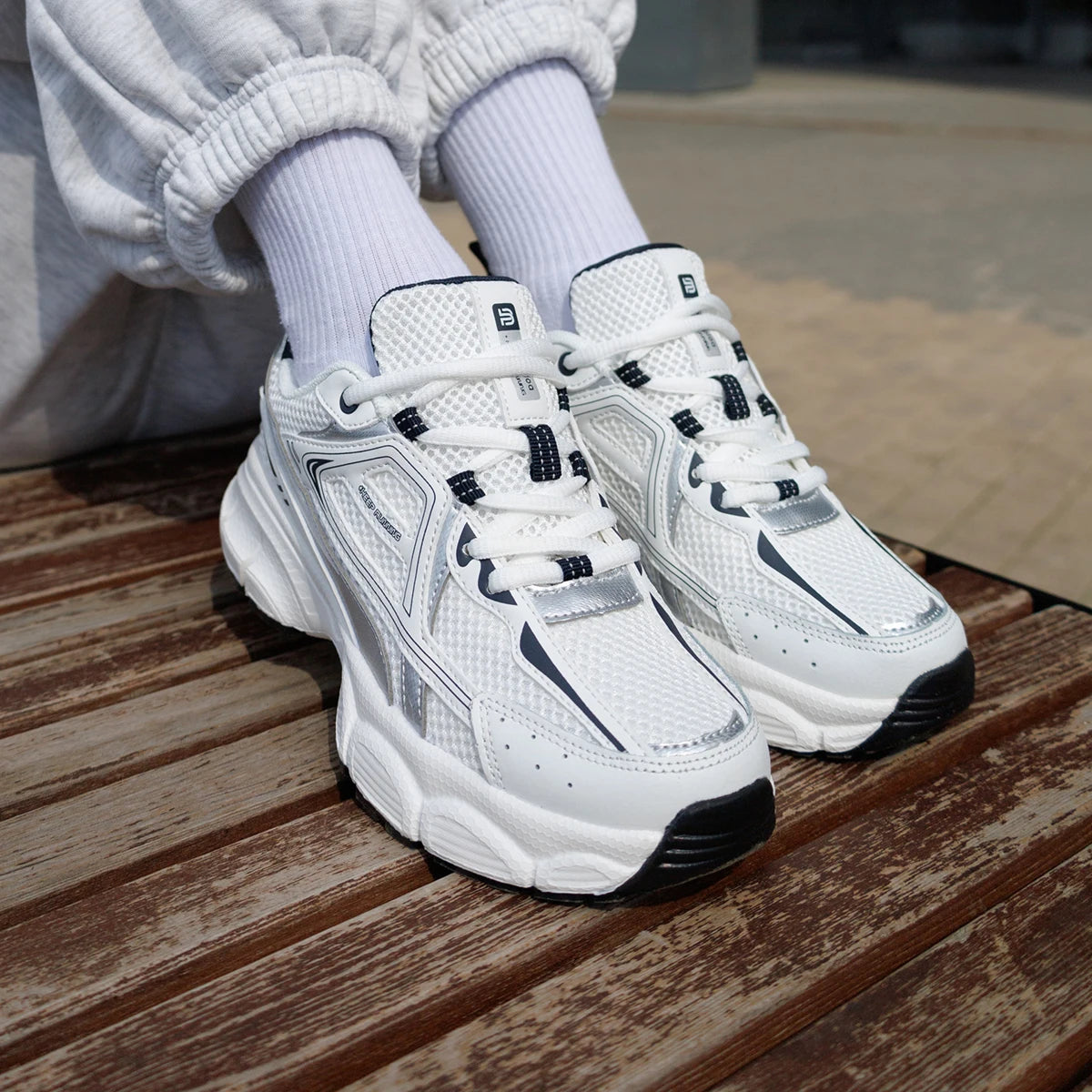 Chunky white sneakers with breathable mesh panels, thick sole, and black accents, styled with white socks and relaxed joggers.