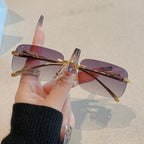 Rimless Y2K rectangle sunglasses with purple gradient lenses and metallic accents, held by a hand with manicured nails.