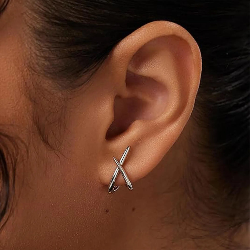 Minimalist silver cross stud earrings worn on the ear, showcasing a sleek, high-polish design.