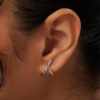 Minimalist silver cross stud earrings worn on the ear, showcasing a sleek, high-polish design.
