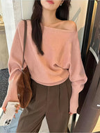 Soft pink LOVORA™ Off-Shoulder Batwing Knit Pullover with relaxed long sleeves, worn off one shoulder, paired with brown pants.