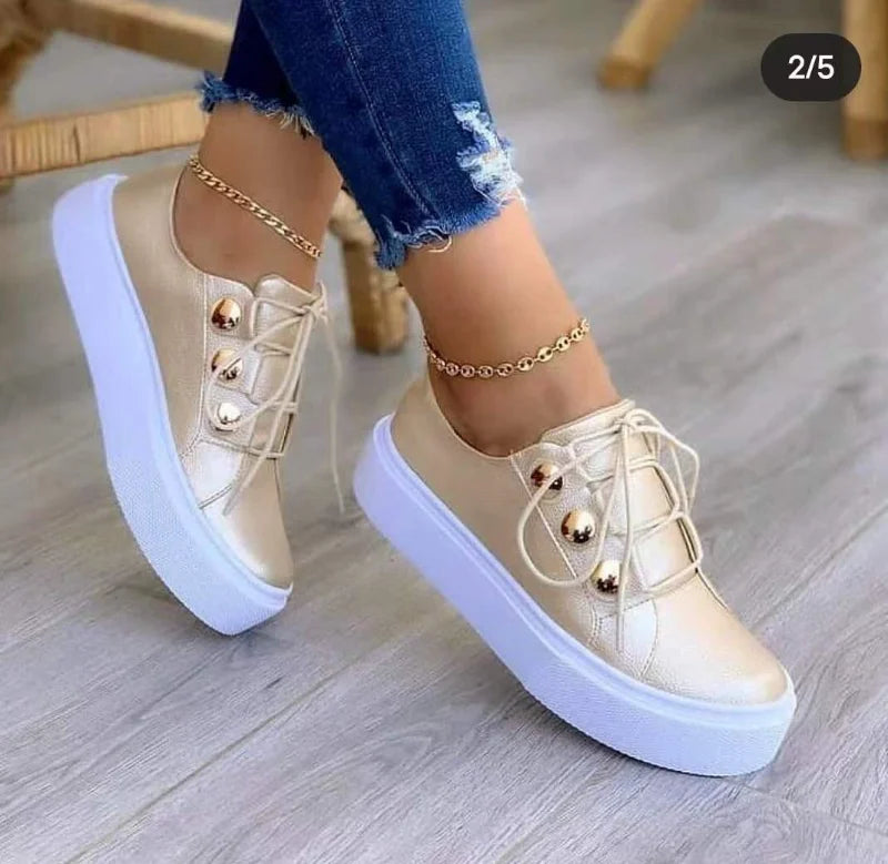 Gold casual sneakers with a thick white platform sole, displayed with distressed blue jeans and an ankle bracelet.