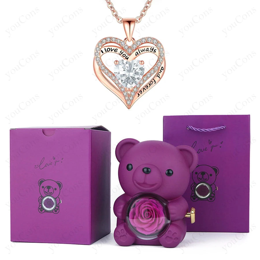 Red heart pendant necklace with "I love you always" inscription, surrounded by sparkling crystals, paired with a purple teddy bear and rose.