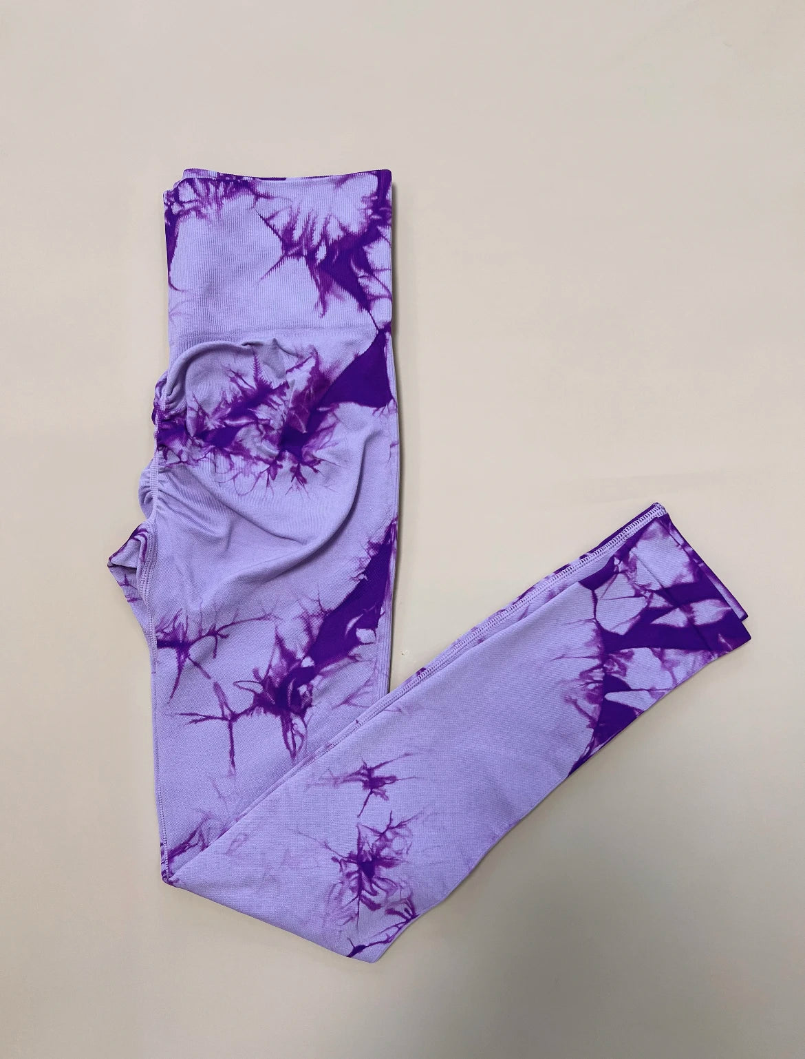 High-waisted leggings in purple with a tie-dye pattern, crafted from a seamless nylon and spandex blend for comfort.