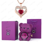 Heart-shaped red pendant necklace with sparkling accents, accompanied by a purple bear holding a preserved rose, in a luxury gift box.