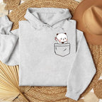 Gray oversized hoodie featuring a cartoon bear peeking from a front pocket, displayed on a textured surface.