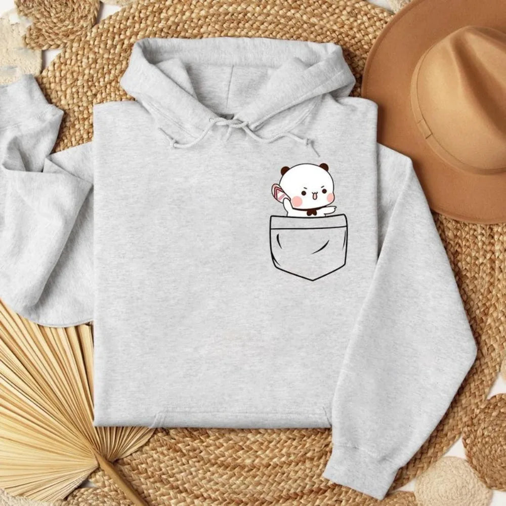 Gray oversized hoodie featuring a cartoon bear peeking from a front pocket, displayed on a textured surface.