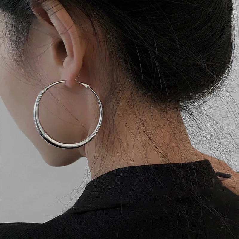 Chunky minimal hoop earrings in high-gloss silver, worn by a model with dark hair styled in a bun.