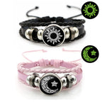 Multi-layered leather bracelet set featuring black and pink bands. Each adorned with a sun or moon token on a braided design.