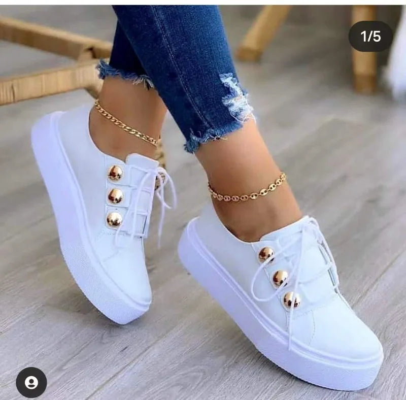 White casual platform sneakers with a smooth eco-leather upper, featuring golden button details and paired with distressed jeans.