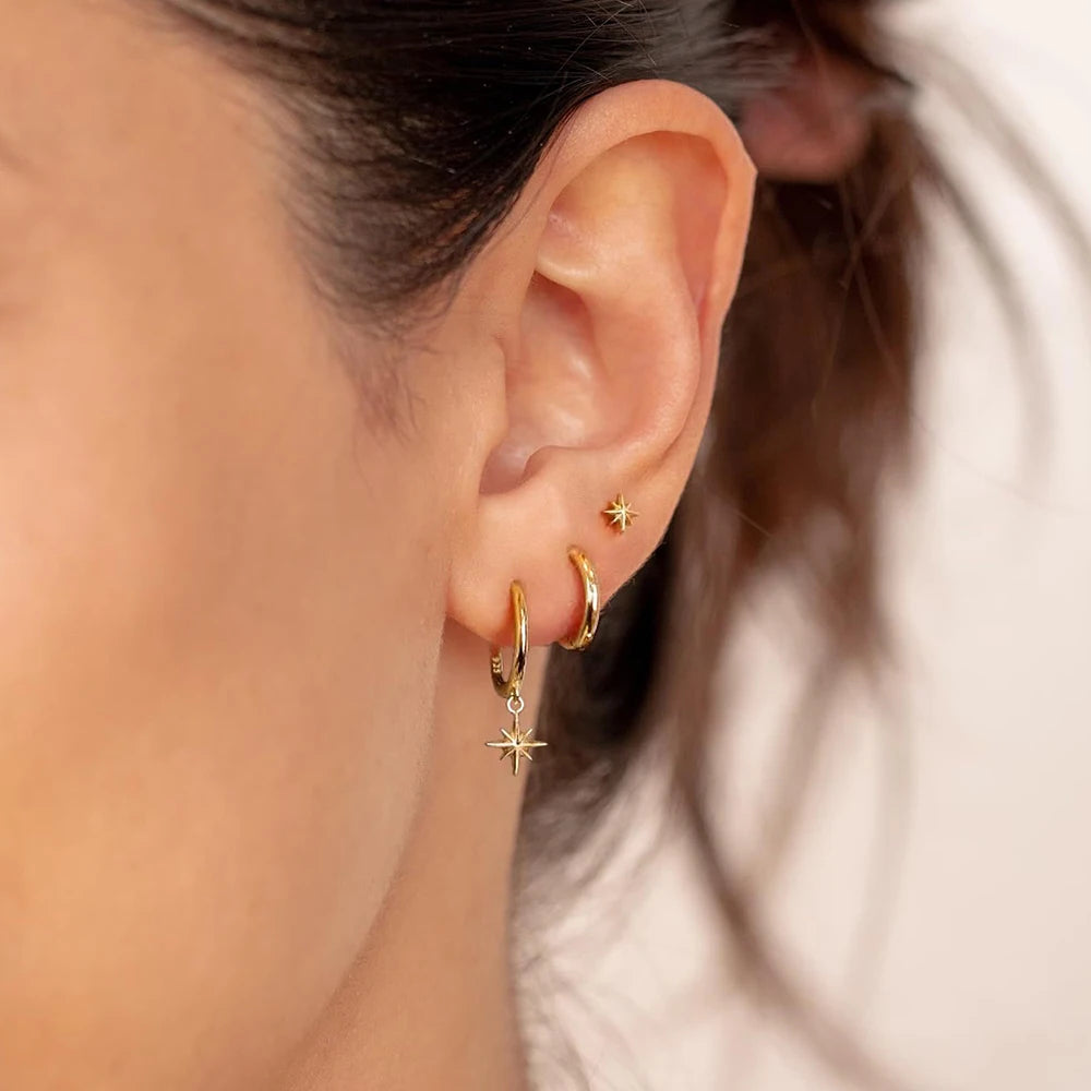 Three-piece earring set featuring high-polish gold hoops, star dangles, and a minimalist stud, worn in the ear.