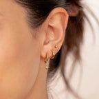 Three-piece earring set featuring high-polish gold hoops, star dangles, and a minimalist stud, worn in the ear.