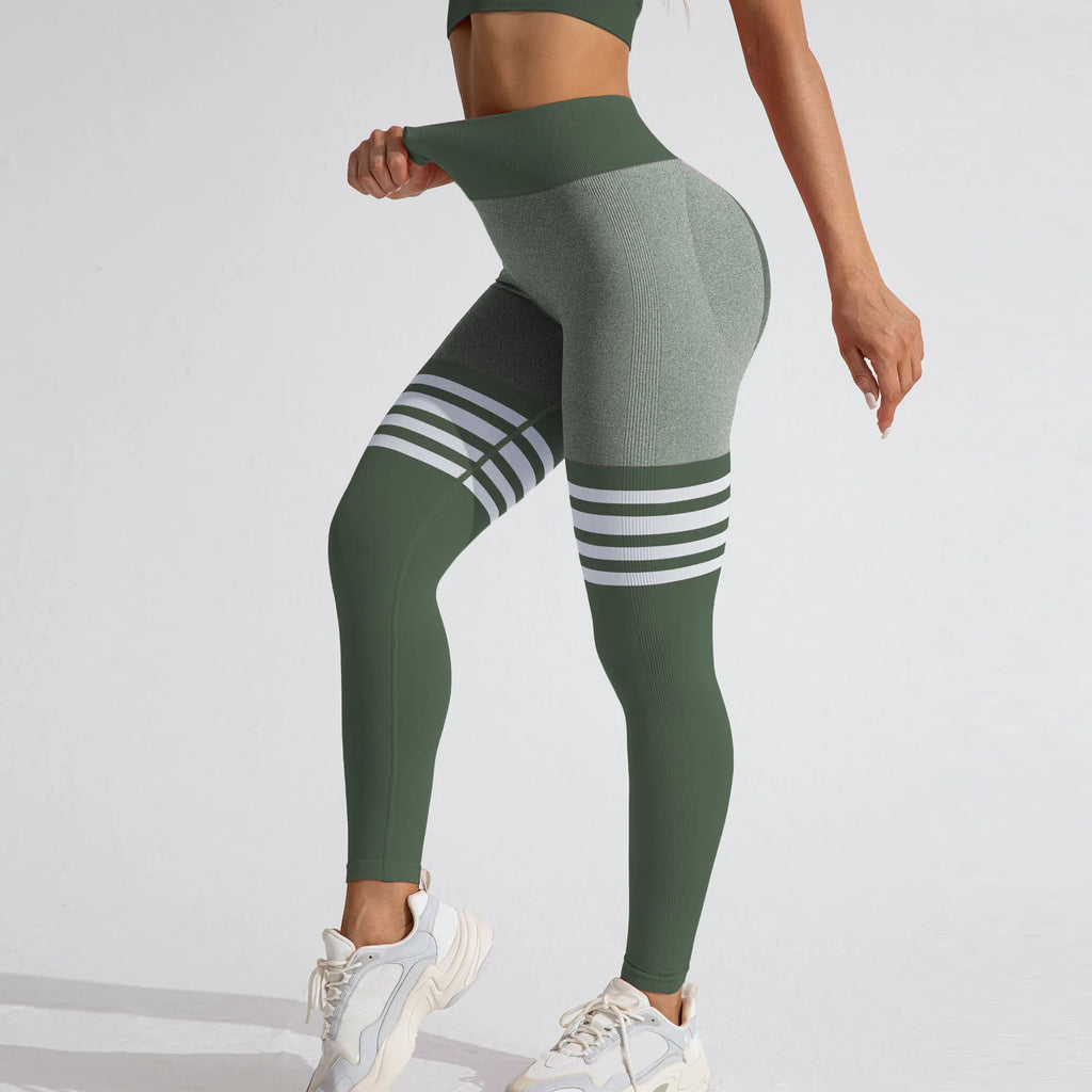 Green high-rise seamless leggings featuring a deep V-back, contrast grey fabric, and white varsity stripes on the thighs.