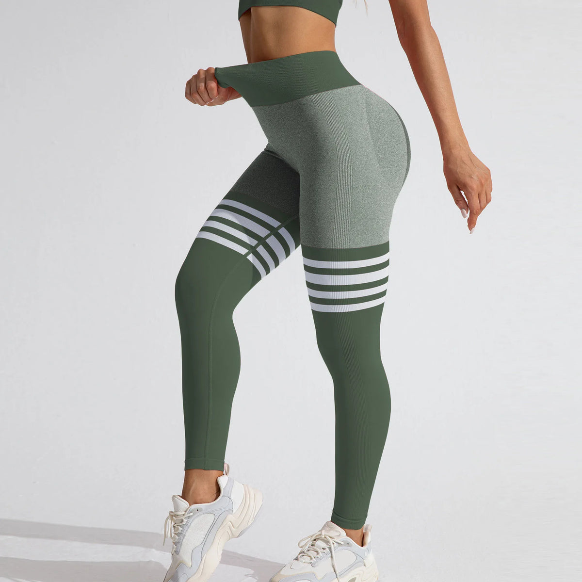 Green high-rise seamless leggings featuring a deep V-back, contrast grey fabric, and white varsity stripes on the thighs.