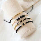 Stack of four bracelets featuring gold-tone beads and glossy black onyx glass stones on a display stand.