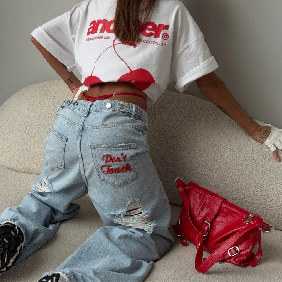 Distressed light blue baggy denim jeans with red "Don't Touch" embroidery, styled high-waisted and oversized.