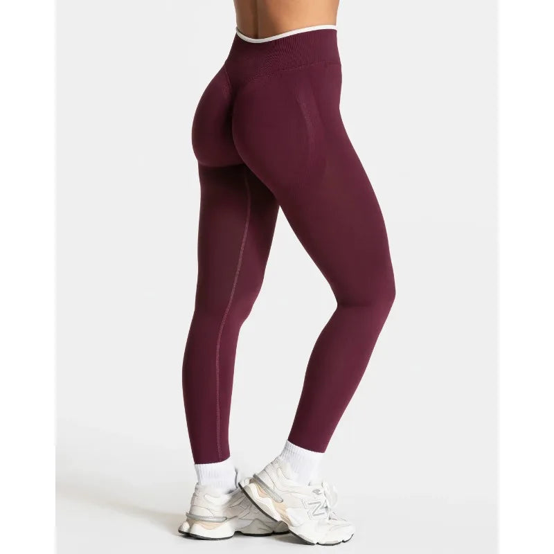 High-waisted, seamless leggings in burgundy with a wide waistband, shown on a model wearing white sneakers.