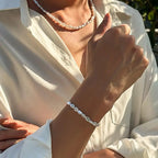 Unisex jewelry set featuring a pearl necklace and bracelet, worn over a white button-up shirt, showcasing a modern design.