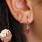Three-piece earring set featuring gold hoop earrings with pink stones, a small marquise stud, and a drop earring with a red teardrop gem.