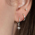 Asymmetric earring set featuring a polished star stud, a hoop, and a dangling star on a model's ear.