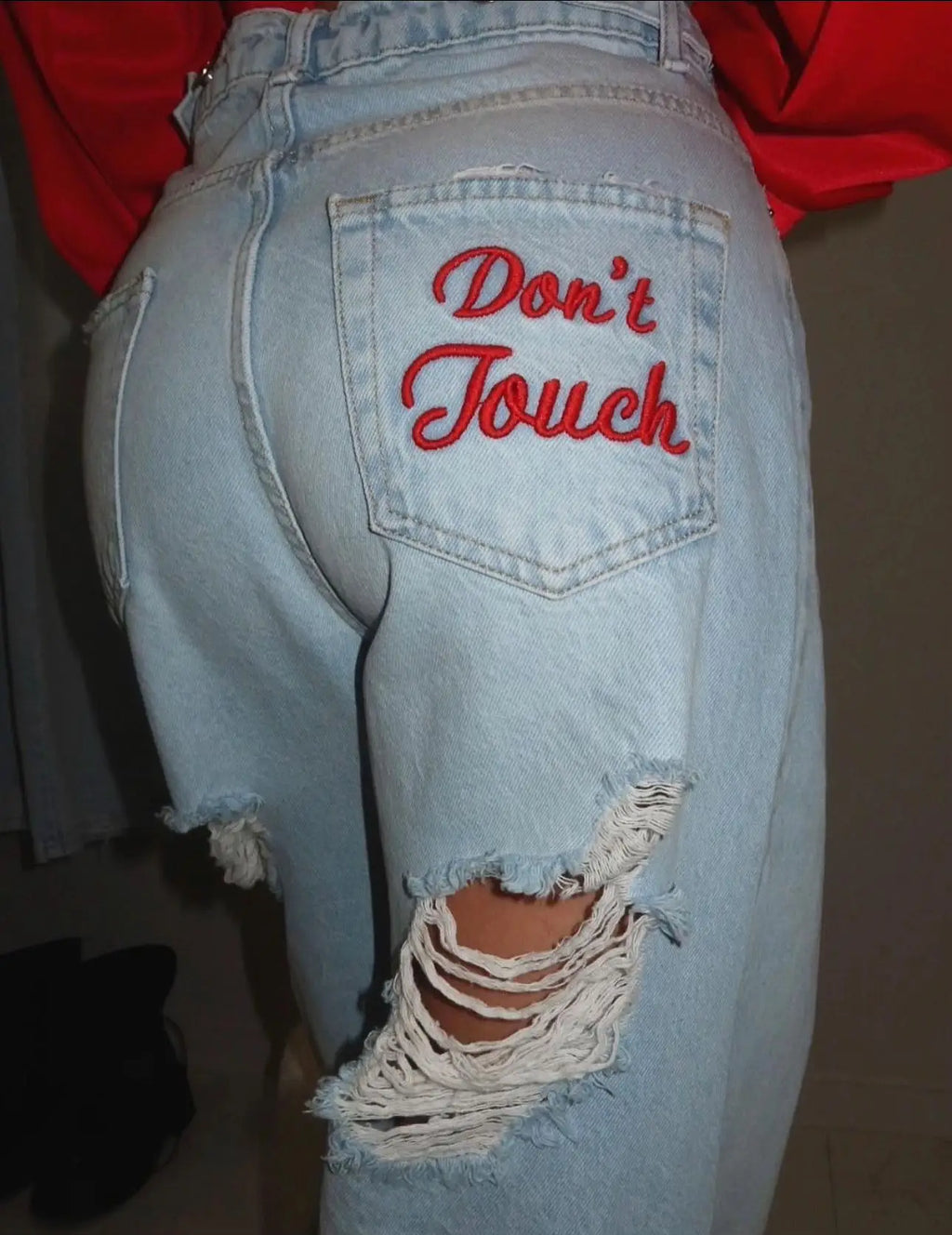 Light blue distressed denim jeans with red embroidered "Don't Touch" detail, oversized baggy fit, and frayed knee rips.