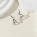 Minimalist silver cross stud earrings with a high-polish finish, displayed on a soft, neutral background.