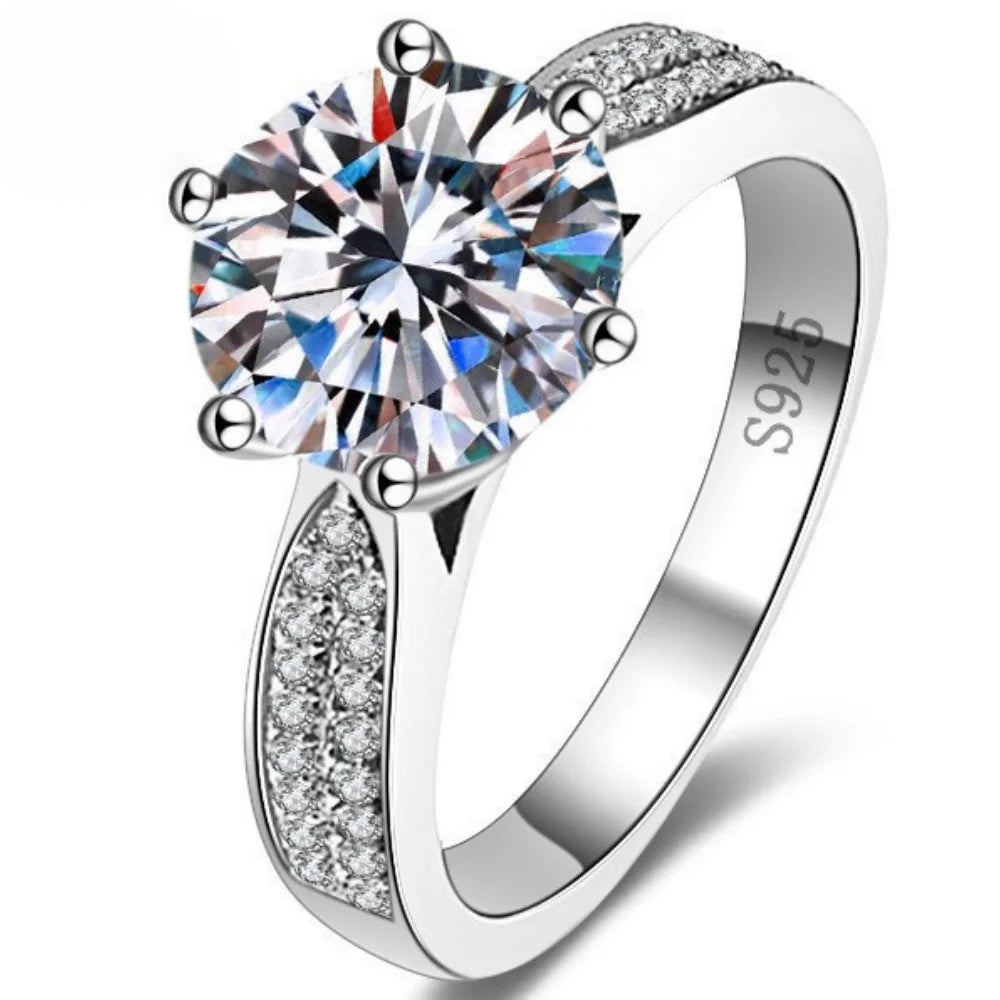 Round-cut Moissanite stone set in a polished 925 sterling silver band, featuring sparkling accents on the shoulders.
