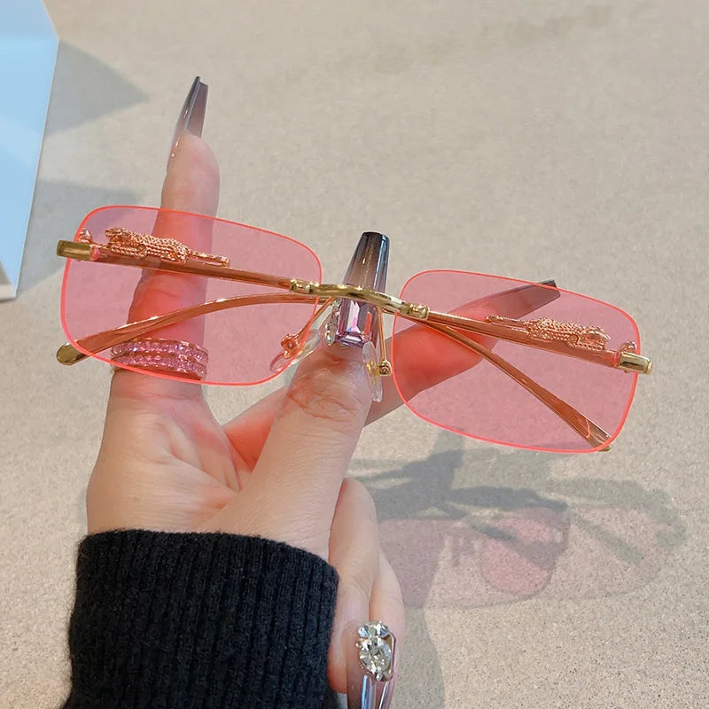 Rimless Y2K rectangle sunglasses with pink gradient lenses and gold metallic accents, held in a hand.