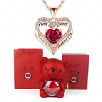 Red heart pendant necklace with rhinestones in a heart shape, alongside a red bear holding a rose, in decorative boxes.