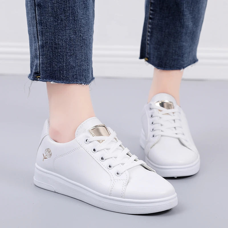 White premium sneakers with floral embroidery, featuring a lace-up design and soft ankle collar, paired with cropped blue denim jeans.