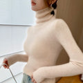 Cream-colored, slim-fit cashmere turtleneck sweater with ribbed texture and high collar, worn casually with a bag.