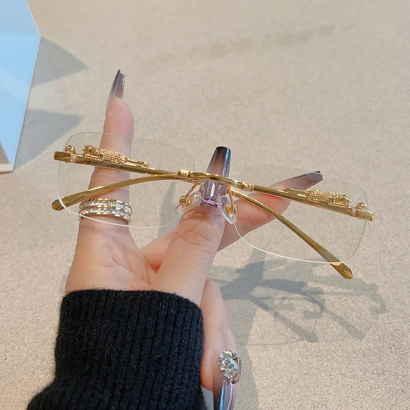 Rimless Y2K rectangle sunglasses with narrow gradient lenses and metallic gold accents, held between the fingers.